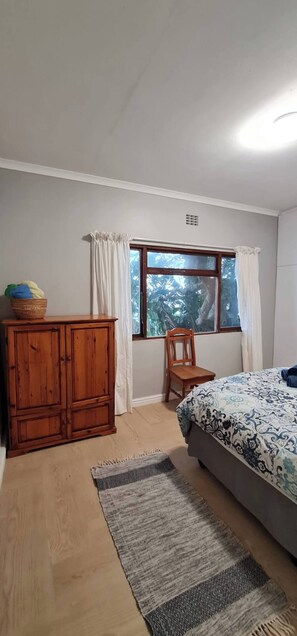A bedroom with a bed, a wooden wardrobe, a chair, a window with curtains, and a rug. - Serene Coastal Retreat with Private Pool in Amatola (Amatola Coastal)