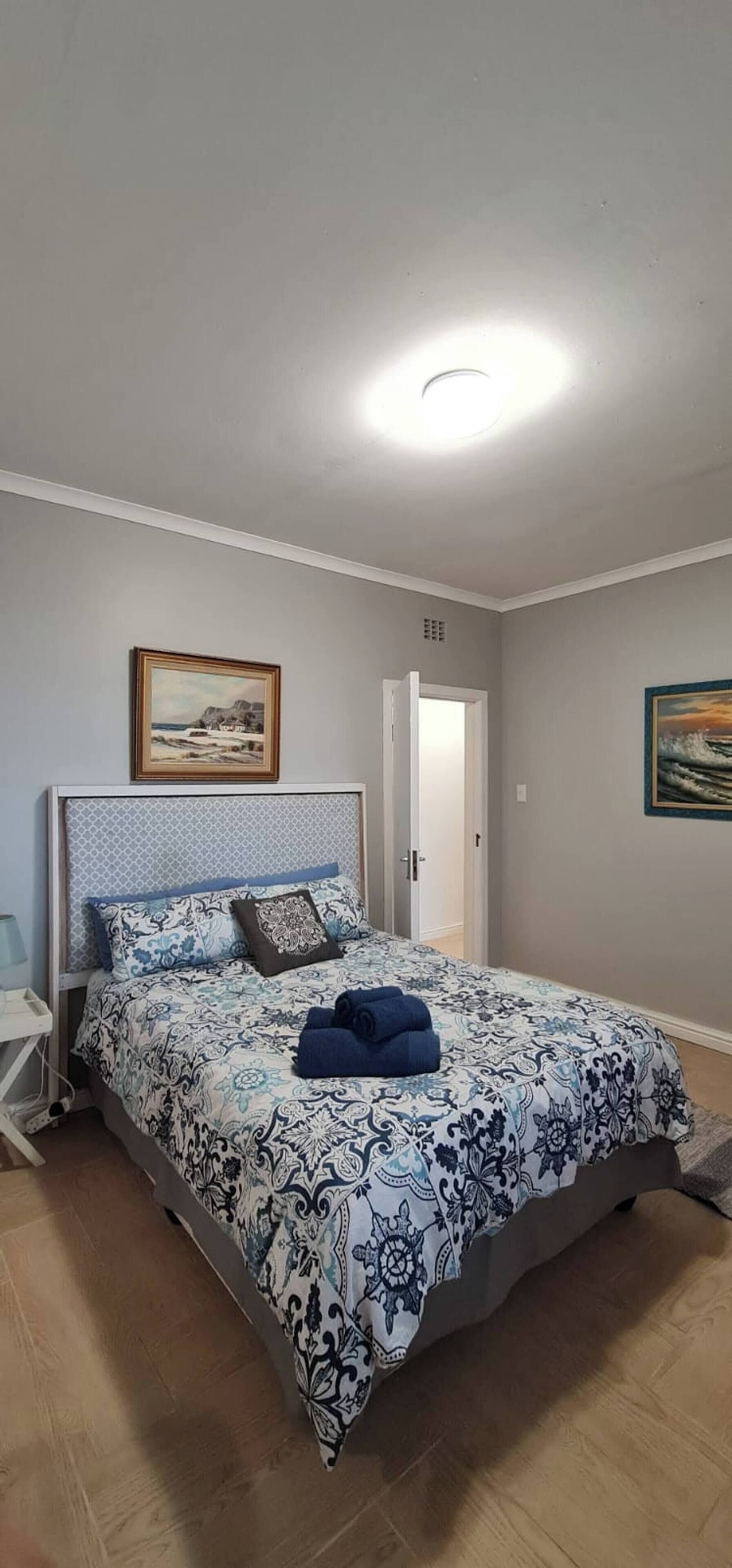 A bedroom with a bed, a nightstand, a door, and a painting on the wall.