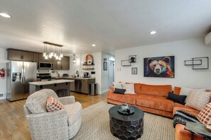 A modern living room with a sofa, coffee table, and kitchen in the background. - Hot Tub/Pool/Near Lake/Whitefish Resort/Dining (Whitefish)
