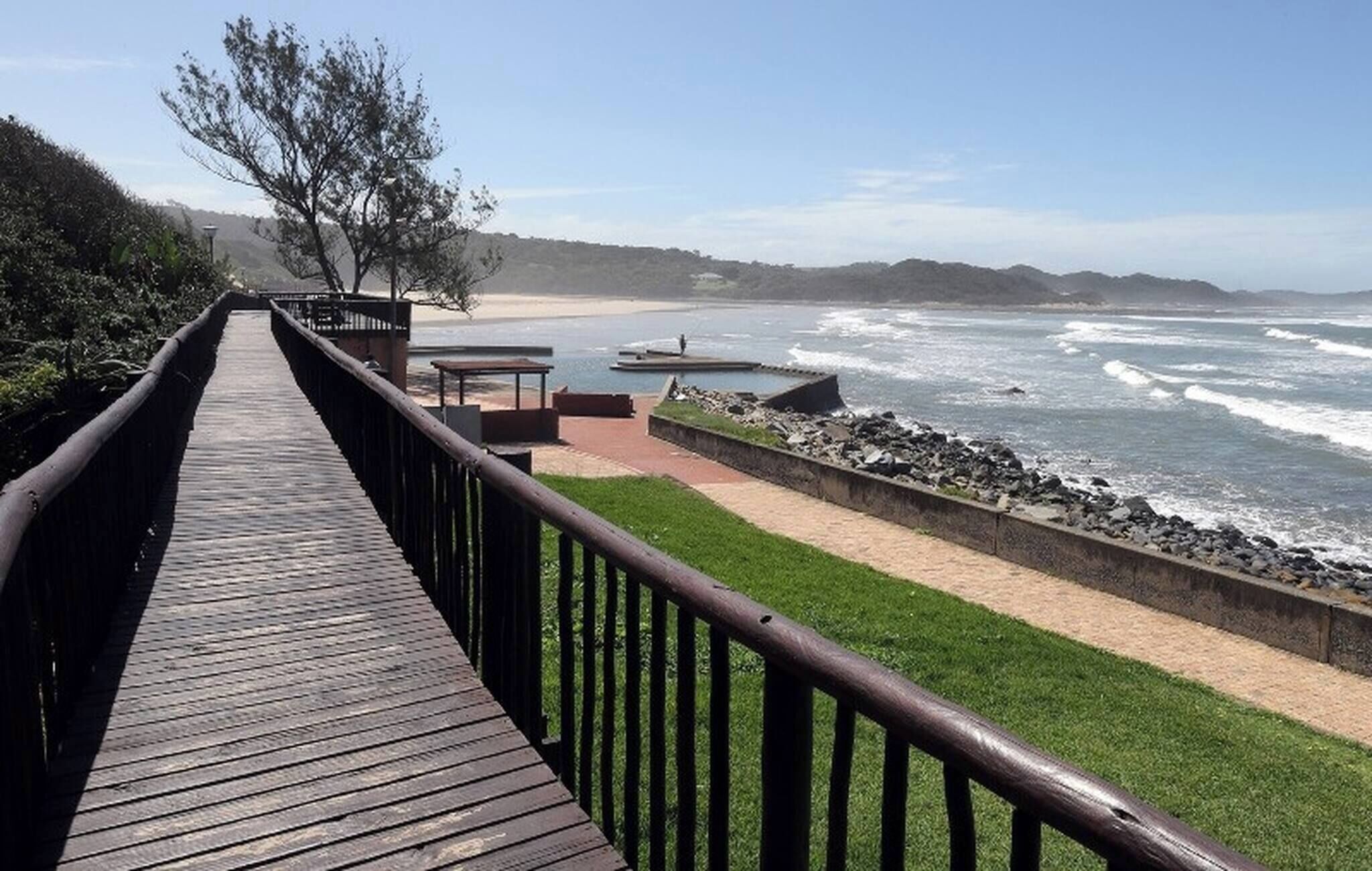 A wooden boardwalk leading to a beach with a rocky shoreline and waves.. Tranquil 1-Bedroom Apartment Near Gonubie Beach