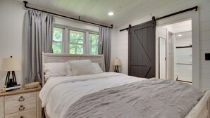 Ein Schlafzimmer mit einem Bett, zwei Nachttischen, einem Fenster mit Vorhängen, einer Schiebetür im Scheunenstil und einem Beistelltisch mit einer Lampe.