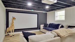 Ein Zimmer mit Projektionsschirm, einer Couch, einer Giraffenskulptur und einem Fenster.