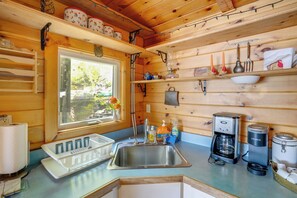 Cocina de cabaña de madera con un lavamanos, cafetera y estanterías.