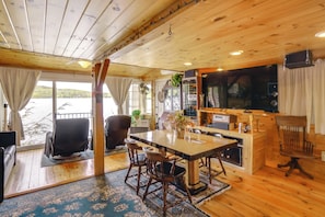 A cabin with a wooden interior, a dining area with a table and chairs, a television, and a view of a lake.