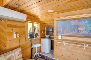 L’intérieur d’une cabane en bois est aménagé avec un ventilateur, un petit réfrigérateur, un évier et un tableau accroché au mur.