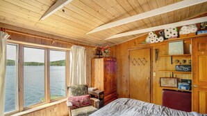 Un dormitorio de cabaña de madera con una ventana grande, una cama, una silla y un armario.