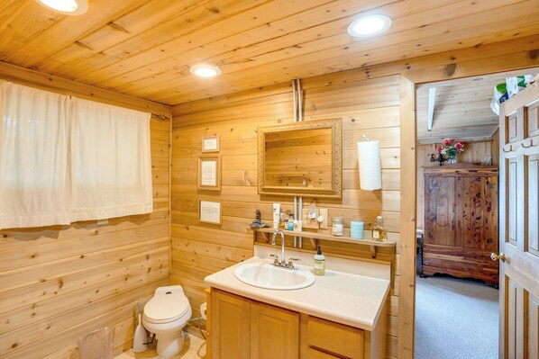 Une salle de bain aux murs lambrissés, équipée d’un lavabo, d’un miroir et de toilettes.