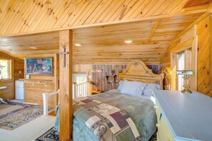 Interior de una cabaña de madera con cama, escritorio, un cuadro en la pared y una pequeña cocina americana.