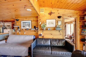 Un acogedor interior de cabaña con una cama, un sofá de cuero, paredes de madera y una ventana.