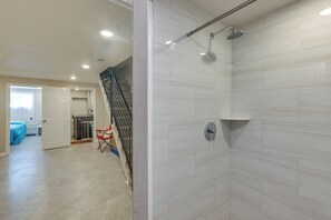Ein modernes Badezimmer mit weißen Fliesen, einer Dusche und einer sichtbaren Treppe, die in einen anderen Raum führt.