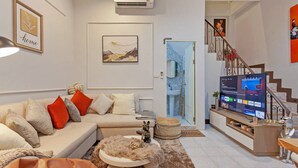 Una sala de estar con sofá, televisor, mesa de centro y una escalera que lleva a un baño.