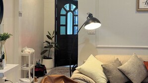 Una sala de estar con un sofá, una lámpara, una planta y una puerta con ventanal.