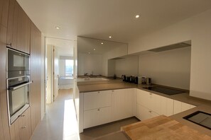 Eine moderne Küche mit eingebauten Geräten, einer großen Kochinsel und Blick zum Wohnbereich.