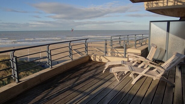 Eine Holzterrasse mit Liegestühlen mit Blick auf einen Strand.