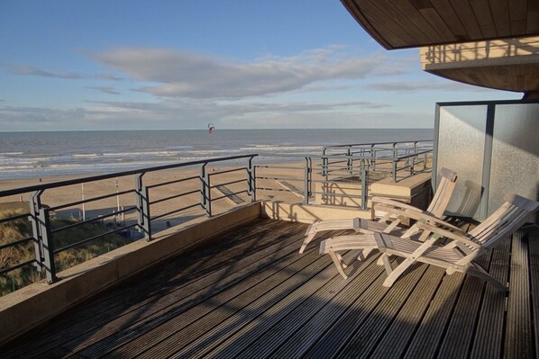 Eine Holzterrasse mit Liegestühlen mit Blick auf einen Strand.