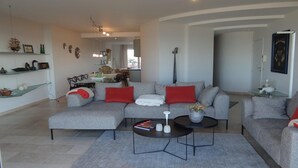 Ein modernes Wohnzimmer mit einer grauen Sofagarnitur, roten Kissen, einem Couchtisch und einem Essbereich im Hintergrund.