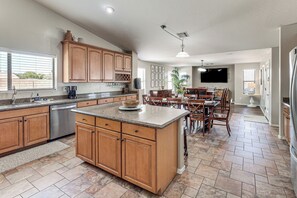 A spacious kitchen with wooden cabinets, a central island, and a dining area with a TV. - Spacious Backyard! Family Haven in San Tan Valley (San Tan Valley)