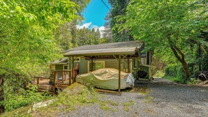 Een rustieke chalet met een overdekte veranda, een grindpad en een dichte bosrand.