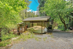 Eine rustikale Holzhütte mit einer überdachten Veranda, einem Schotterweg und dichtem Wald drumherum.
