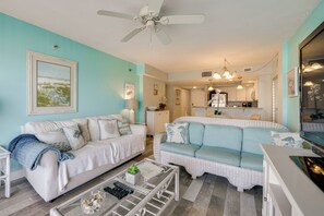 Ein Wohnzimmer mit einem weißen Sofa, einem blauen Sofa, einem Couchtisch und einem Deckenventilator.