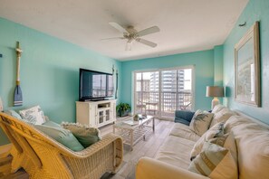 Ein Wohnzimmer mit Fernseher, Korbmöbeln, einem Balkon mit Blick und einem Deckenventilator.