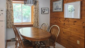 A wooden-paneled room with a round dining table, chairs, a refrigerator, and a window with curtains. - Kenway Ranch: Family Retreat Near Acadia Trails (Southwest Harbor)