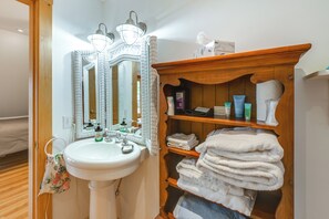 Ein Badezimmer mit weißem Waschbecken, einem Spiegel mit dekorativem Rahmen und einer Holztrennwand mit Handtüchern und Toilettenartikeln.
