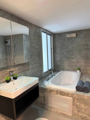 Une salle de bain moderne avec un grand miroir, deux lavabos, une baignoire et une petite plante en pot.