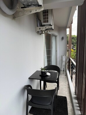 Un balcon avec une table, des chaises, un pot de fleurs et un appareil de climatisation.