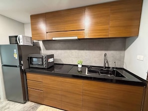 A compact kitchen with wooden cabinets, a black countertop, a built-in microwave, a toaster, and a stainless steel sink. - Stylish Loft Apartment Near Fisherman’s Village (Bo Put)