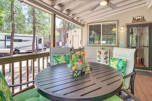 A covered outdoor deck with a round table, chairs, and a birdcage with flowers. - Fairways, Fishing & Forest Fun! Show Low Retreat (Show Low)