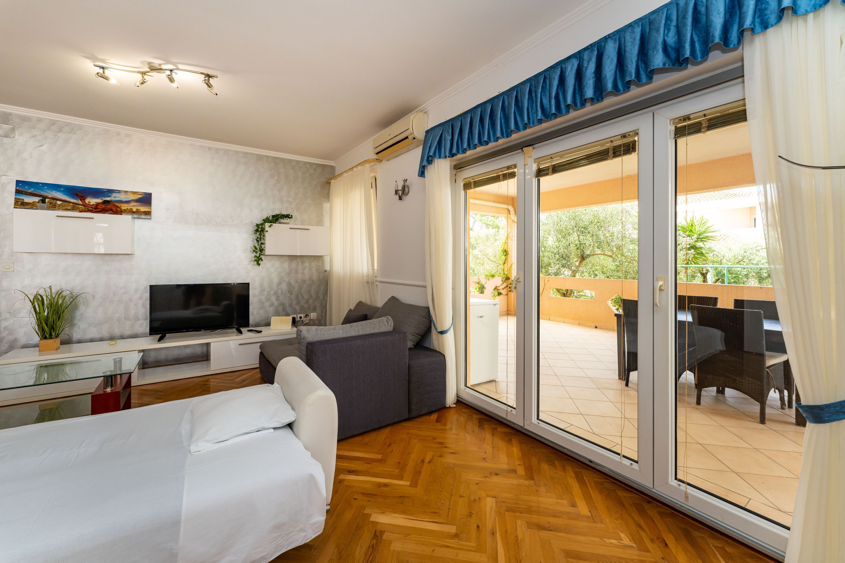 Een moderne kamer met een bed, een televisie, een bank en een glazen schuifdeur naar een terras.