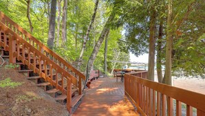A wooden deck leading to a dock, surrounded by tall trees. - Glen Arbor Home w/ Glen Lake Access & Shared Dock! (Glen Arbor)