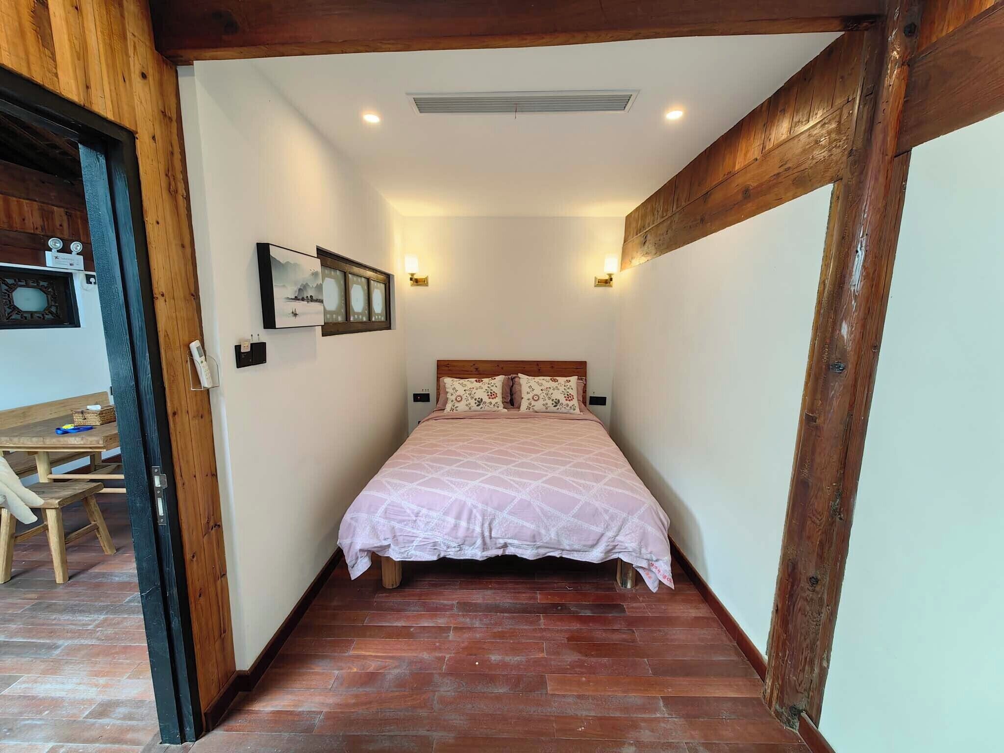 Quarto pequeno com uma cama, vigas de madeira, uma mesa e um quadro na parede.