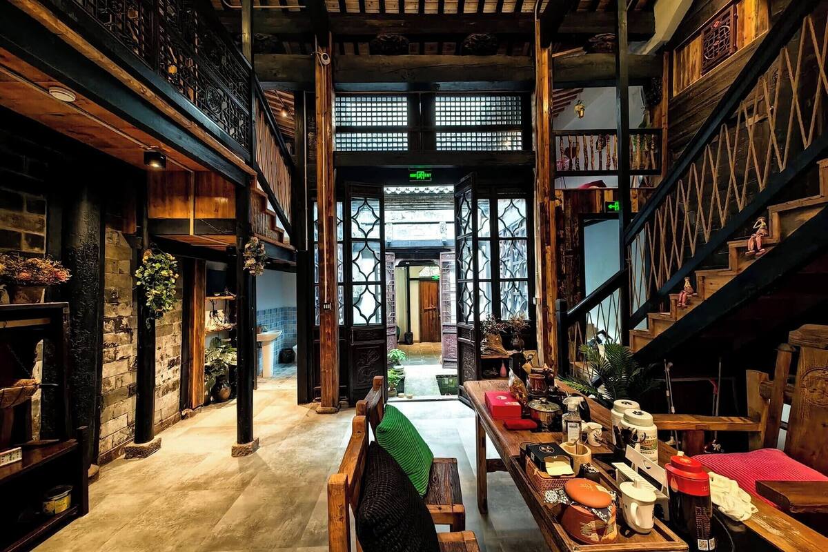 A traditional interior with wooden beams, a central staircase, and a view to the outside.