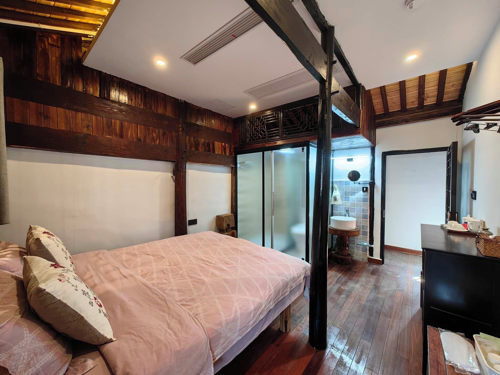 Camera da letto con un letto grande, pannelli in legno, una porta in vetro che conduce al bagno e un televisore su un tavolo di legno.