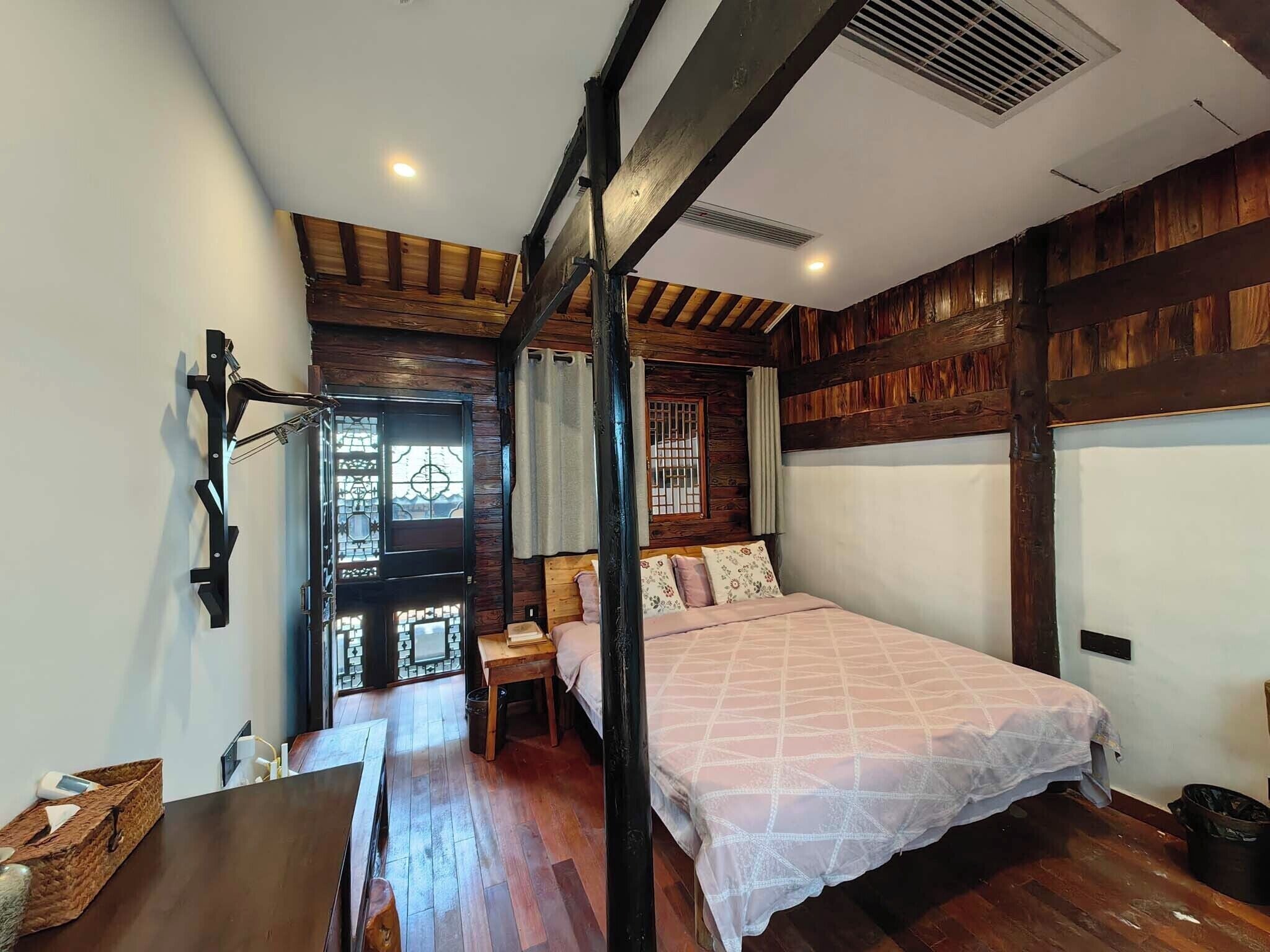A bedroom with a wooden ceiling, a bed with a patterned bedspread, a nightstand, and a window with a view.