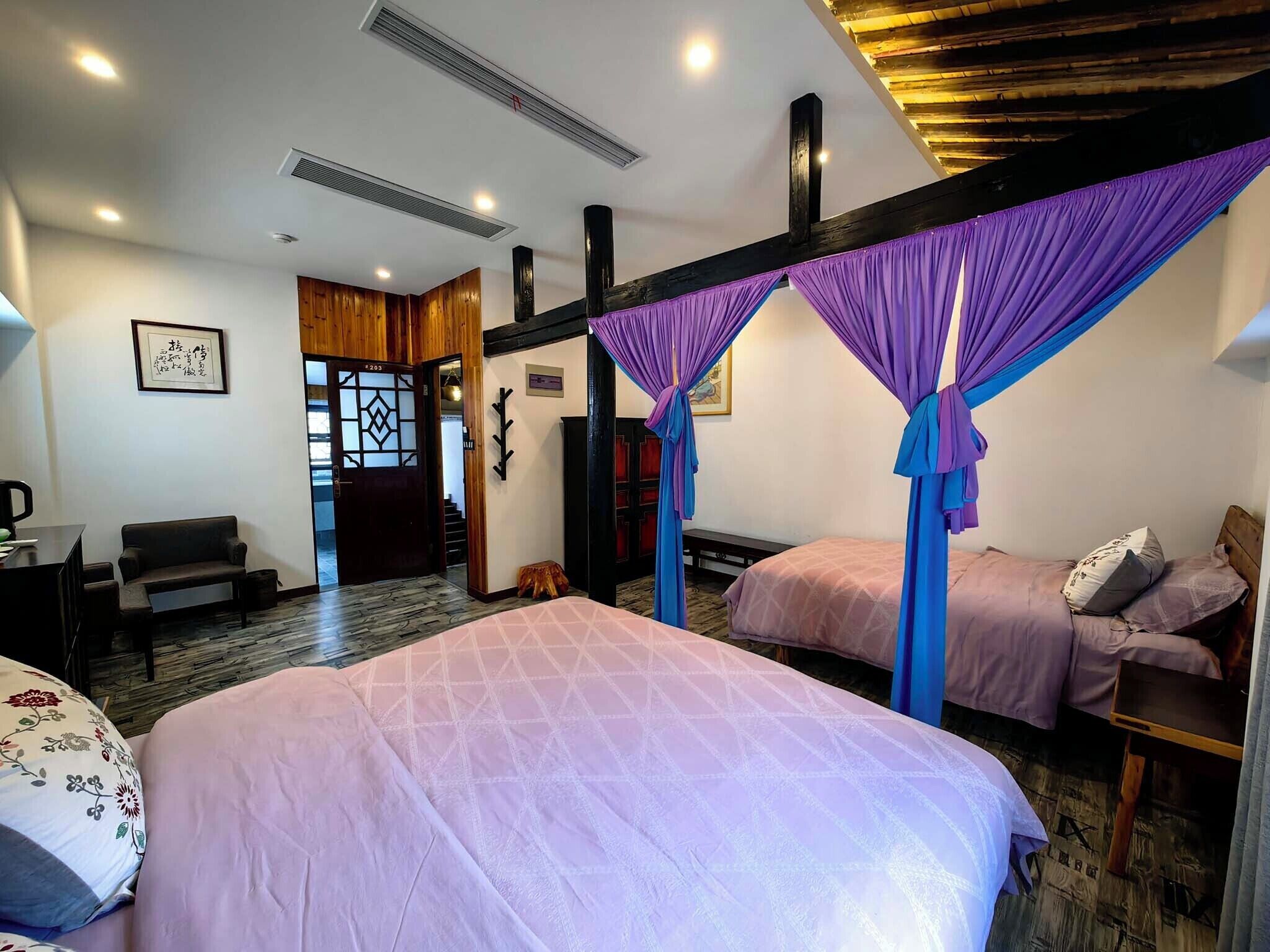 Quarto de hotel com duas camas, um sofá, uma escrivaninha e teto de madeira.