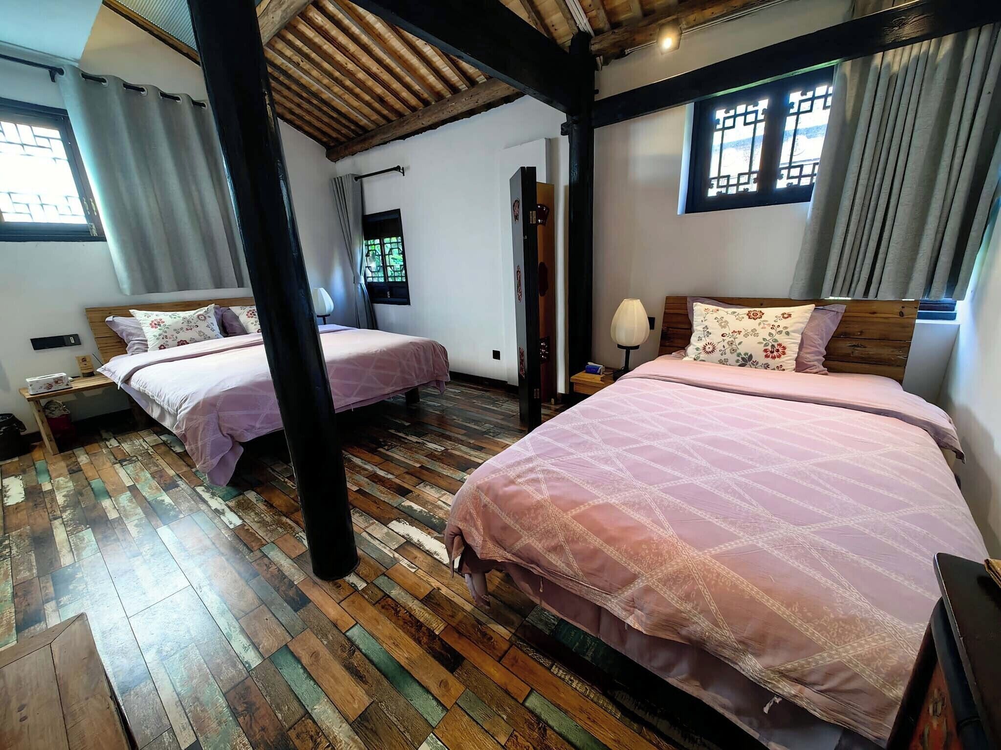 A room with two beds, wooden flooring, a wooden ceiling, and a window with a view.