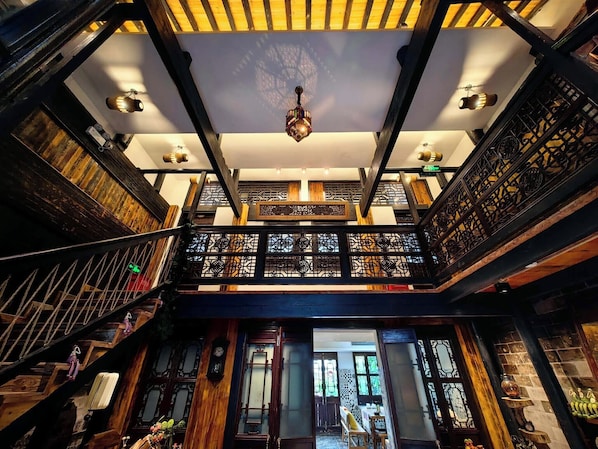 Un interior con varios niveles, vigas de madera, una escalera y una barandilla decorativa.