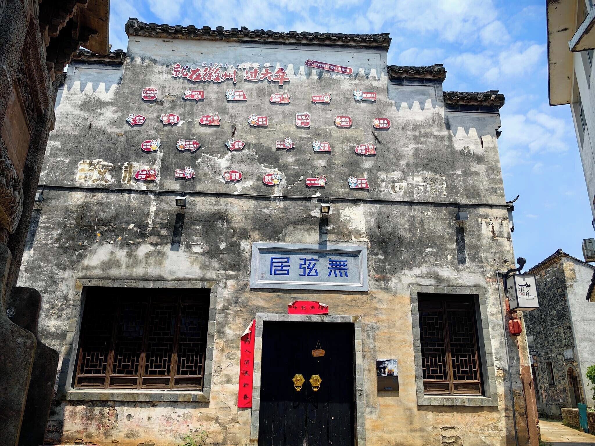 Un bâtiment orné d’une enseigne sur laquelle sont apposés de nombreux autocollants, d’une grande enseigne bleue au-dessus de l’entrée et d’une porte noire traditionnelle dotée de poignées dorées.