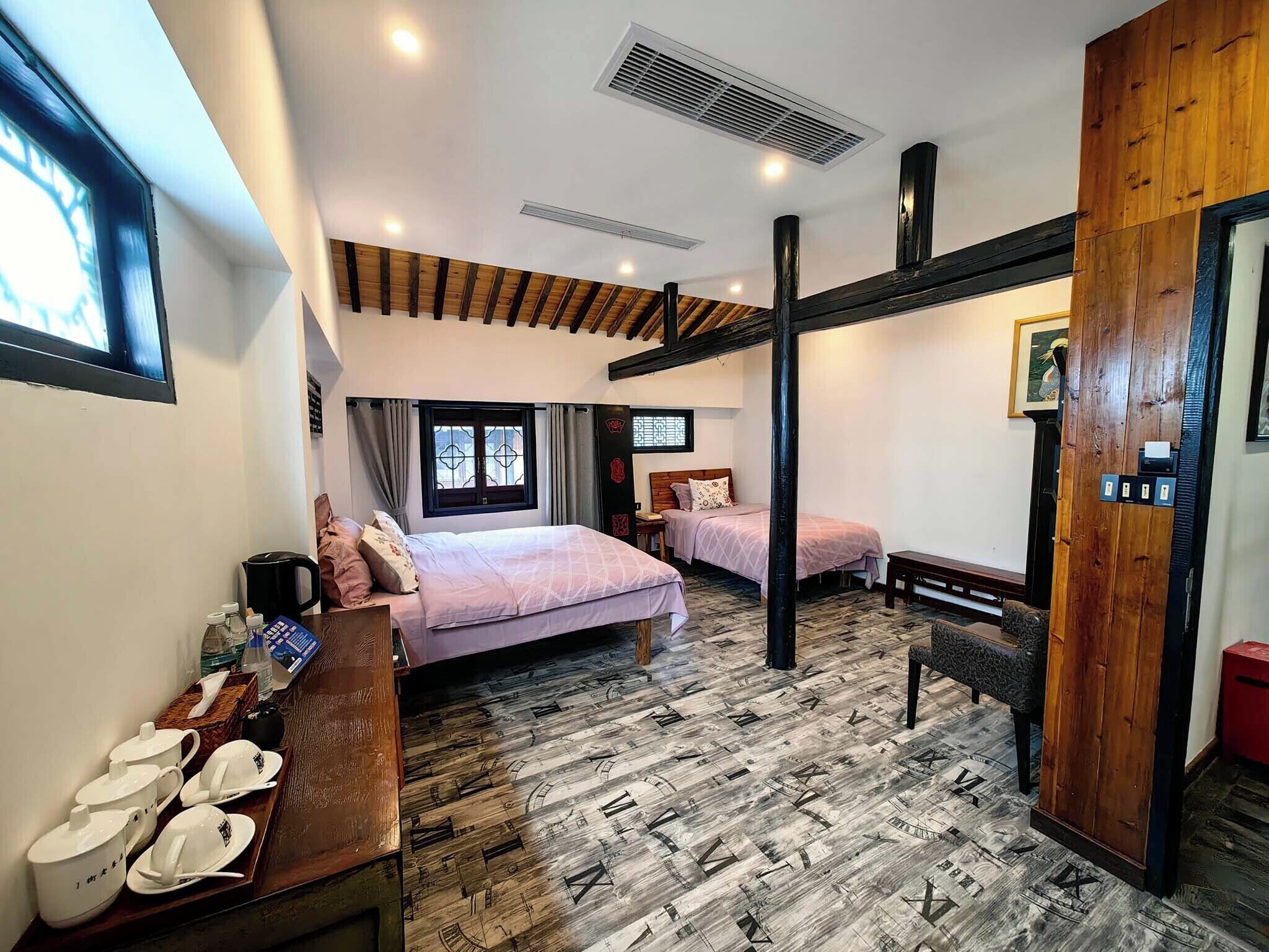 A bedroom with two beds, a wooden floor with a clock pattern, a window with curtains, and a wooden door.
