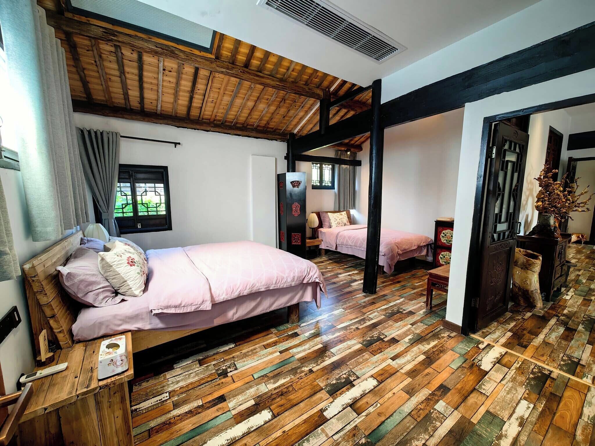 Quarto com teto de madeira, cama com colcha rosa, piso de madeira e janela com cortinas.