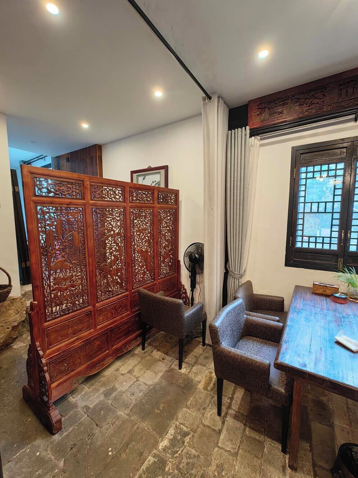 A traditional room with a wooden partition, a fan, a table, and a window with a view.