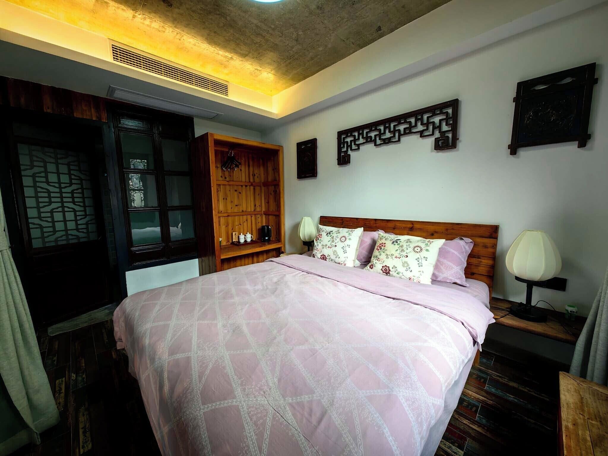 Une chambre à coucher comprenant un lit, une armoire en bois, des œuvres d’art décoratives au mur et une table de chevet avec une lampe.