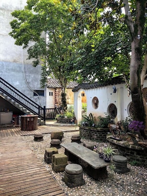 A courtyard with a wooden deck, stone benches, a small brick structure, and a tree providing shade. - Dream Country Qiankou Resort (Huangshan)