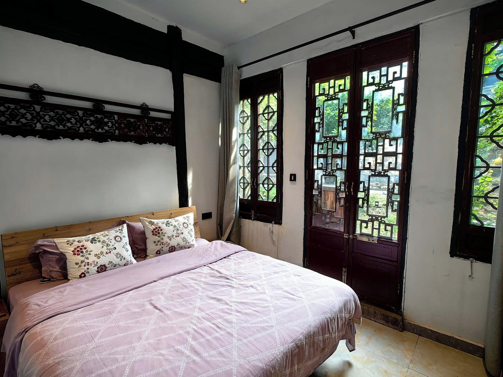 Quarto com cama, cabeceira de madeira, janela com grades metálicas decorativas e vista para o verde lá fora.