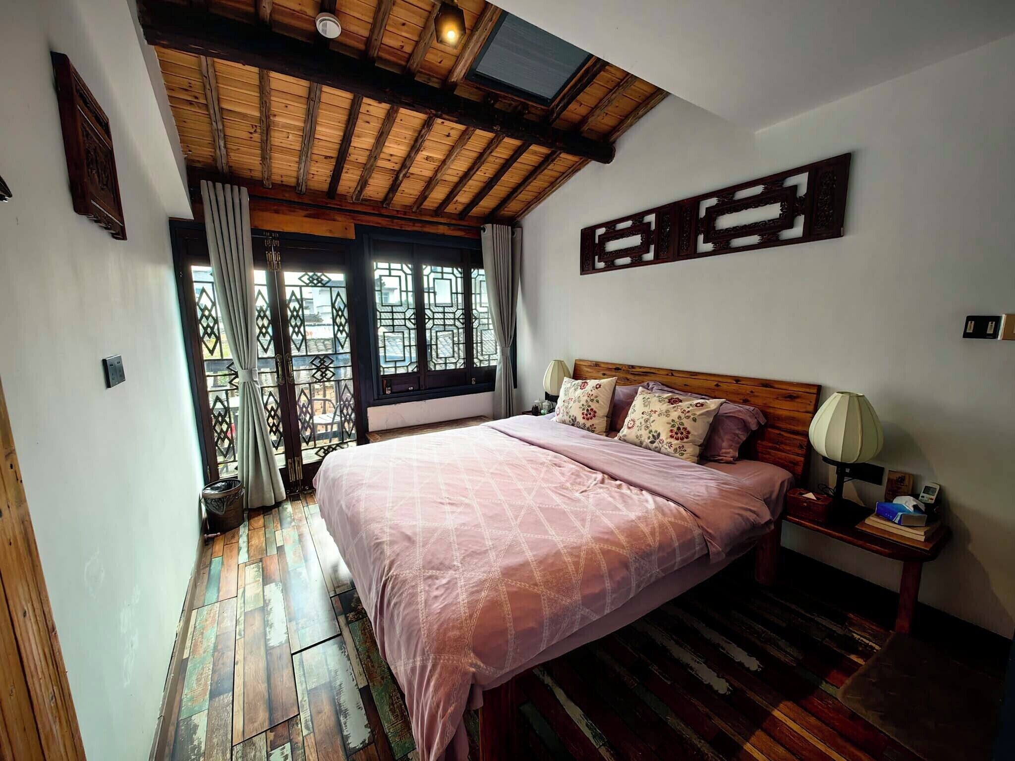A bedroom with a large bed, wooden flooring, a ceiling fan, and a window with a view.