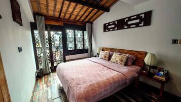 A bedroom with a large bed, wooden flooring, a ceiling fan, and a window with a view.