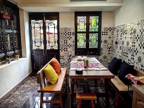 Uma área de refeições com uma mesa de madeira, bancos e uma janela com painéis de vidro decorativos.
